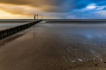 Fototapeta premium Beautiful sunset over wooden breakwater at the edge of Baltic sea