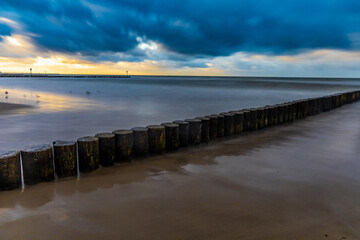 Beautiful sunset over wooden breakwater at the edge of Baltic sea