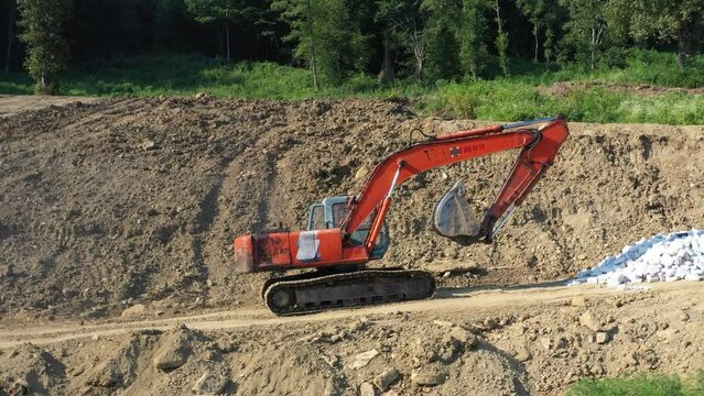 Earthmoving equipment. A red excavator is digging the ground. The bucket of the excavator scoops up the soil against the background of nature. Slow motion.