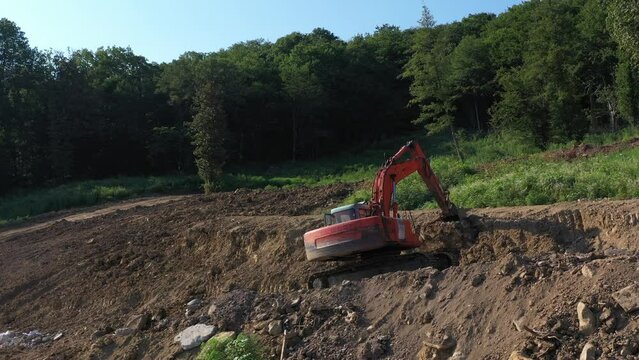 Earthmoving equipment. A red excavator is digging the ground. The bucket of the excavator scoops up the soil against the background of nature. Slow motion.