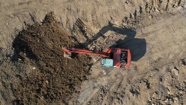 Earthmoving equipment. A red excavator is digging the ground. The bucket of the excavator scoops up the soil against the background of nature. Slow motion.