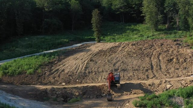 Earthmoving equipment. A red excavator is digging the ground. The bucket of the excavator scoops up the soil against the background of nature. Slow motion.