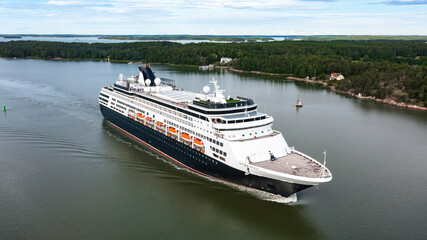 Obraz premium Luxury cruise vessel making way ahead in beautiful Finnish archipelago. Narrow fairway and shoreline proximity. Low altitude aerial forward view.