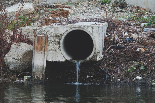 Dirty water flows out of the old rusty pipe without cleaning. Pollution of natural water bodies. Kingfisher bird in corner