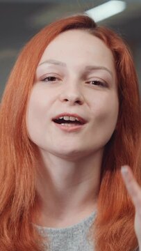 Vertical Screen: Emotional woman with red hair talking to webcam and gesturing during online meeting. Closeup of young female expressing opinion. Concept of communication