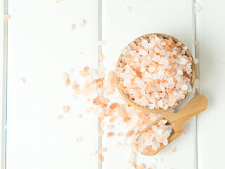 pink sea salt, heap of sea salt in a wooden bowl and scoop on a light wooden background close-up