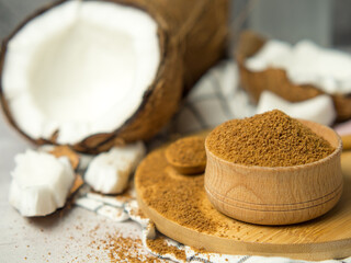 Coconut palm brown sugar in a wooden bowl and spoon and half of the coconut fruit on a gray concrete background.
