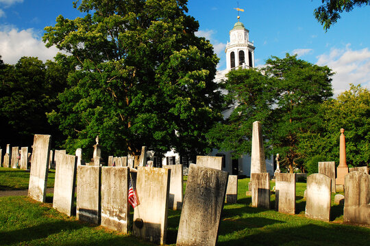 A historic  graveyard and tombstones surround a classic church in New England