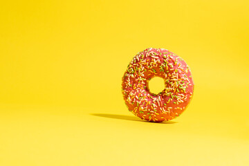Fototapeta na wymiar Pink donut with multicolored sprinkles on yellow background. Creative food background