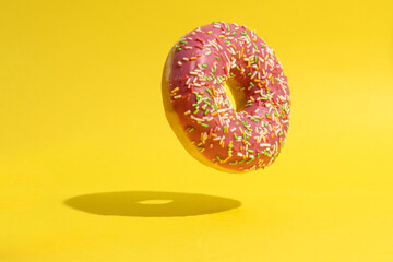 Fototapeta na wymiar Levitating pink donut on yellow background. Creative food background