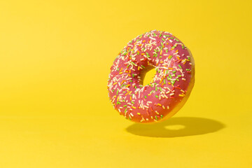 Fototapeta na wymiar Levitating pink donut on yellow background. Creative food background
