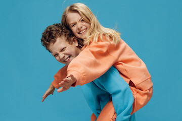 two cute, joyful children in multi-colored sweaters stand on a blue background, a boy rolls a happy...