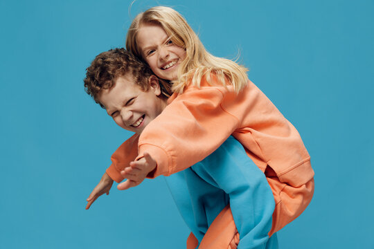 two cute, joyful children in multi-colored sweaters stand on a blue background, a boy rolls a happy girl on his back. The theme of children's friendship and relationships