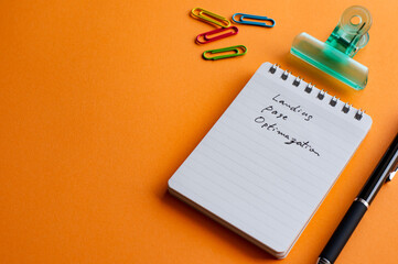 There is a notebook with the word Landing Page Optimization. It's placed on a color background.
