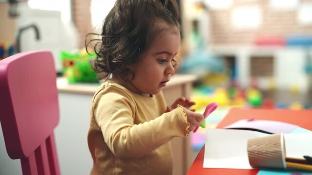 Adorable hispanic girl student holding scissors at kindergarten