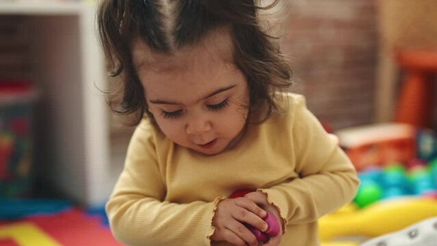 Adorable hispanic girl playing with maths puzzle game sitting on floor at kindergarten