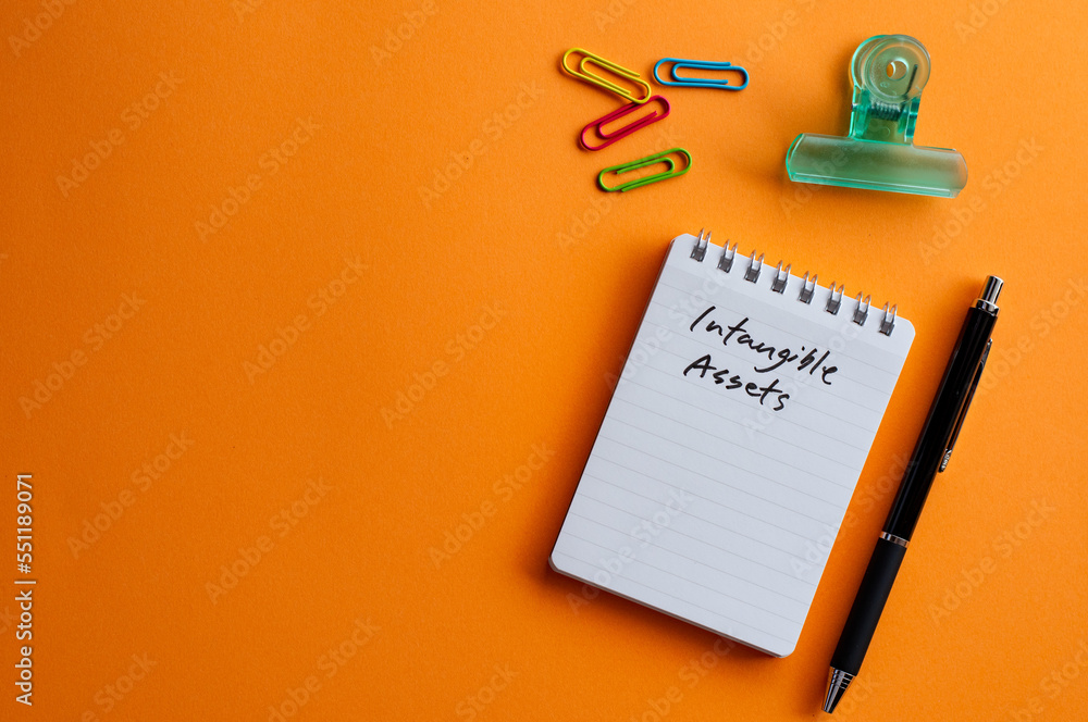 Poster there is a notebook with the word intangible assets. it's placed on a color background.