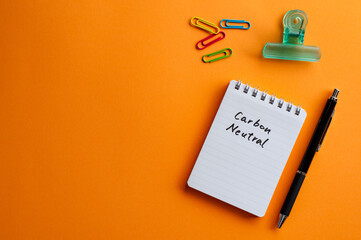 There is a notebook with the word carbon neutral. It's placed on a color background.