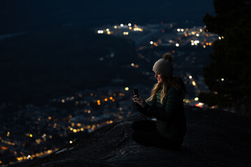 Woman looking at phone overlooking city at night