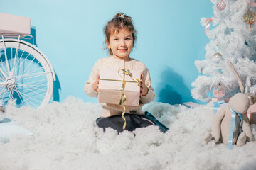 Smiling merry, positive little girl getting surprise present box, sitting on soft cozy wadding carpet like cloud against