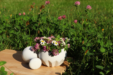 Ceramic mortar with pestle, different wildflowers and herbs on wooden board in meadow. Space for text