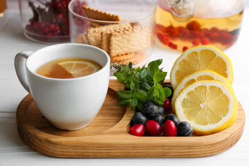 Cup with delicious immunity boosting tea and ingredients on white wooden table