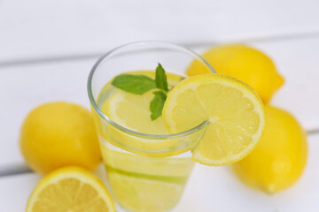 Glass of water with lemons and mint on white wooden table, closeup