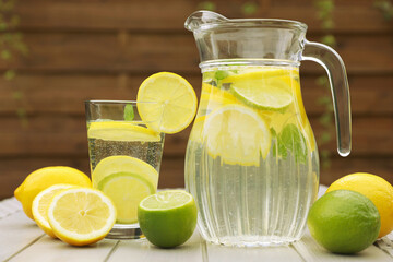 Water with lemons and limes on white wooden table outdoors