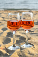 Glasses of tasty rose wine on sand near sea