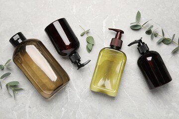 Shampoo bottles and leaves on white textured table, flat lay