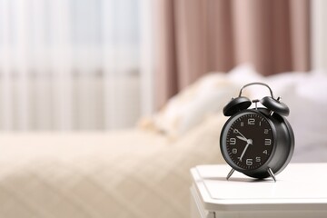 Black alarm clock on white nightstand indoors. Space for text
