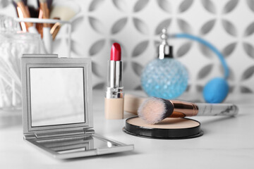 Stylish pocket mirror and cosmetic products on white table