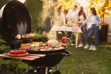 Group of friends having party outdoors. Focus on barbecue grill with food. Space for text - Powered by Adobe