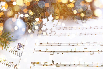 Fir branches, decorative snowflake and light blue balls on Christmas music sheets, closeup. Bokeh...