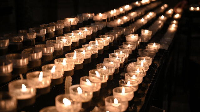 Many candles burning in cathedral. Votive candles glows on All saints day. Prayer lighted candles in a Catholic church.  