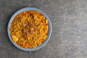 spicy fried instant noodle with egg and fried shallots on top on grey plate