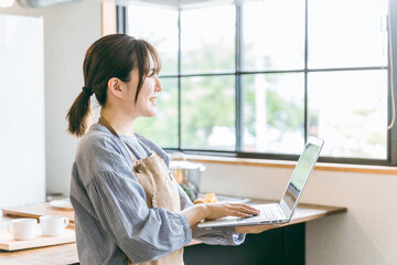 キッチンでノートパソコンを使ってを見るカフェスタッフのアジア人女性
