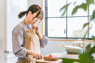 キッチンで料理が苦手でトマトを切るのに悩むアジア人女性
