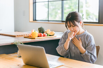 ノートパソコンで仕事をしながら喘息・咳で困るアジア人女性
