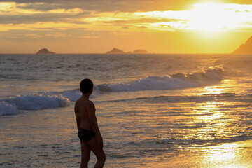 Fototapeta premium Rio de Janeiro, RJ, Brazil - December 03, 2022 - People in silhouette at sunset walk on Ipanema Beach