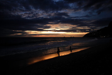 Rio de Janeiro, RJ, Brazil - December 03, 2022 - People in silhouette at sunset walk on Ipanema Beach
