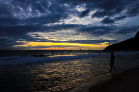 Rio de Janeiro, RJ, Brazil - December 03, 2022 - People in silhouette at sunset walk on Ipanema Beach