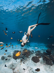 Beautiful freediver lady with fins glides underwater with tropical fishes in transparent ocean