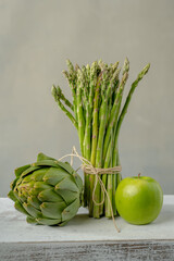 A bunch of fresh asparagus, apple, artichoke on a white box made of wood