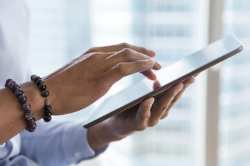 Dark skinned business man using online app, virtual service on tablet computer, touching, swiping touchscreen, typing, shopping on Internet. Cropped shot, hand holding gadget close up