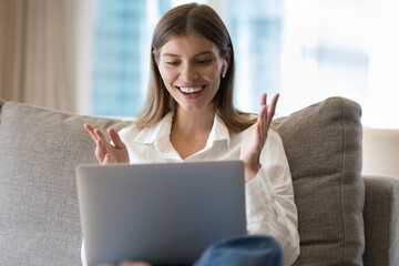 Excited cheerful pretty 30s laptop user woman staring at display, shouting for joy, gasping, laughing, holding head in amazement, surprise, getting good awesome news, sitting on home couch