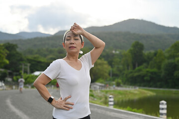 A gray-haired woman in her 60s wipes the sweat on her forehead after exercising by jogging.