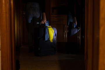 A Ukrainian woman stands near the door of an apartment with a suitcase and a flag of Ukraine and a...