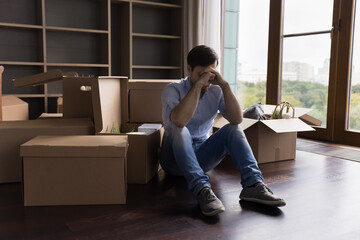 Tired unhappy bankrupt man moving out from apartment, sitting at pile of paper cardboard relocation...