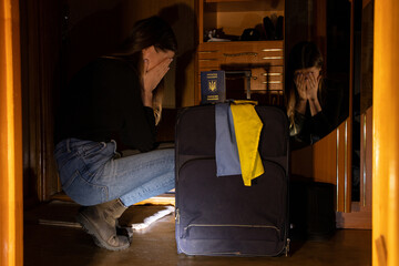 Ukrainian woman crying near a suitcase with the flag of Ukraine and a passport in the dark without...